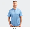 A men's polo in light blue, featuring a collar, buttons, and a logo. Model is smiling and standing.