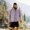 A full zip jacket in light grey, worn by a man outdoors, surrounded by trees and mountains. The jacket has a logo.