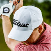 A white cap with a branded logo, designed for performance in golf, featuring a curved peak and breathable fabric.