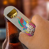 A drink bottle opener in silver is being used to remove a bottle cap from a cold drink. The design features vibrant, colourful patterns.