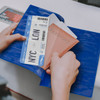 A blue vinyl travel wallet containing a passport and airline tickets. Hands are holding the wallet open.
