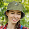 A faded green bucket hat with a logo, worn by a woman in a natural outdoor setting.