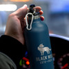 A drink bottle in matte blue with a silver top and a logo featuring a wolf, held by a hand.