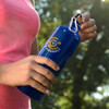 A drink bottle in vibrant blue, featuring a clip and a logo, held by a person in activewear outdoors.