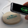 A round, beige wireless charger with a logo, connected to a smartphone displaying a charging icon.