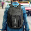 A person wearing a denim jacket carries a grey and black Selwyn Backpack with a logo on the front.