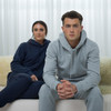 A pair of unisex sweatpants in navy and grey, styled with matching hoodies, on individuals seated indoors.