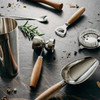 A cocktail shaker, jigger, spoon, strainer, and a bottle opener with wooden handles and stainless steel elements.