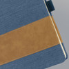 A denim notebook featuring a blue fabric cover with a brown leatherette stripe and stitching detail.