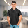 A man wearing a black polo shirt with a logo, standing in an office setting.
