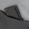 A smartphone in a grey fabric pocket of a black backpack with a zip.