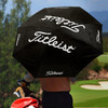 A black double canopy umbrella with a logo, held by a person near a golf course.