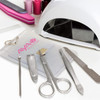 A vinyl manicure set with silver tools in a clear pouch, alongside a white nail lamp and pink nail files.
