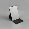 A compact mirror with a sleek black stand, featuring a reflective surface and a minimalist design.