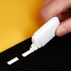 A correction tape dispenser in white being used to apply tape on a black surface against a yellow background.