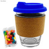 A glass coffee cup with a royal blue lid and a cork band, accompanied by a packet of colourful jelly beans.