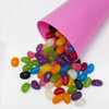 A pink party cup tipped over, spilling a variety of colourful jelly beans in numerous shapes and sizes.