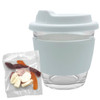 A glass coffee cup with a light blue silicone sleeve, accompanied by a pack of mixed jelly lollies in various colours.
