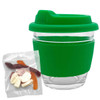 A green glass coffee cup with a silicone lid and sleeve, accompanied by a packet of mixed lollies in various colours.