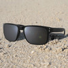 A pair of black sunglasses resting on sandy ground, featuring a simple design and grey lenses.