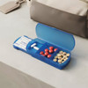 A blue travel pill box with compartments containing various pills, resting on a flat surface beside a bag.