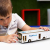 A white wooden bus model is being examined by a child, featuring a branding logo on the side.