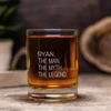 A glass tumbler filled with amber liquid, featuring a clear branding logo, set on a wooden surface.