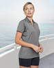A grey ladies' polo shirt with contrast teal detailing, featuring a logo, modeled by a woman near water.