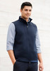 A navy softshell vest with a zip front, worn over a light blue shirt, includes a branding logo.