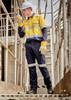 A worker in a yellow and navy work shirt and cargo pants, wearing gloves and a hard hat, on a metal staircase.