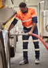 A worker in orange and navy bio motion taped stretch jeans operates equipment in a work environment, featuring reflective strips.