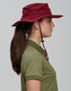 A maroon surf hat with a wide brim, featuring a chin strap and ventilation holes, worn by a person with long hair.