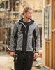 A work jacket in grey and black, featuring a hood and a logo, worn by a model on a construction site.