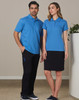 A man and woman standing together, wearing matching blue polo shirts. The man pairs his top with black cargo pants, while the woman wears a black skirt.