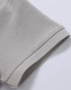A close-up of a light grey polo shirt's sleeve, showcasing the pique texture and stitch detailing.