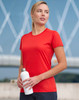 A woman wearing a red short-sleeved performance t-shirt holds a white drink bottle, set against a blurred outdoor background.