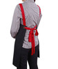 A black canvas bib apron with red straps tied at the back, worn by a person in a checkered shirt.