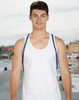 A model wearing a plain white tank top with blue straps, standing by a waterfront. The background features a dock and buildings.
