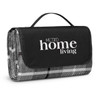 A folded picnic blanket with a black carrying handle, featuring a grey and white pattern and a logo.