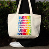 A zippered cotton canvas shopper tote in natural colour with a rainbow of text highlighting various positive themes.