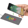 A grey fabric wireless charging pad with a smartphone being charged. The pad features a logo.