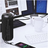 A black rugged fabric waterproof Bluetooth speaker positioned beside a smartphone and a cup in a workspace setting.