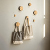 Two recycled cotton twill tote bags in grey and beige hanging on wooden pegs against a light wall.