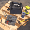 A black Arctic Zone Titan Deep Freeze Lunch Cooler on a wooden pallet with tools like wrenches, a hammer, and a drill nearby.