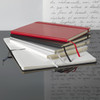 A collection of hard-bound journals in red, black, and silver, featuring ribbon bookmarks and lined pages.
