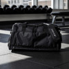 A black duffle bag with multiple zippered compartments and a logo, resting on a gym floor.
