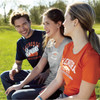 A group of three people wearing short sleeve t-shirts in navy, grey, and orange, featuring logos on the front.