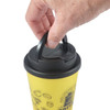 A yellow coffee mug with a black handle lid, featuring a hand gripping the lid.