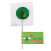A green lollipop wrapped in plastic with a white stick, accompanied by a branded label.