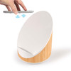 A wireless charger and speaker with a white top and bamboo base. A smartphone is held above the charger.